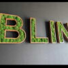 Wood-framed 3D letters spelling BLIN filled with green ball moss mounted on a dark gray wall