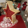 Natural wood star frame filled with red reindeer moss, angled side view on a holiday table runner.