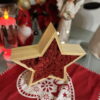Wooden star frame filled with red reindeer moss, standing on a red festive table mat with holiday ornaments.