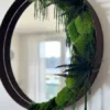 Round wall mirror with dark wooden frame decorated with preserved green ball moss and fern fronds