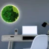 Round illuminated green moss wall art glowing above modern office desk with laptop and chair