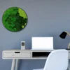 Round mixed moss wall art with a black frame mounted above a modern desk with a laptop and lamp.