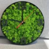 Round wall clock with green reindeer moss, black numeric markers, and black rim resting on a gray fabric surface.