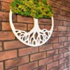 Angled view of round tree of life wall art with white frame and green moss foliage on a brick wall.
