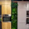 Vertical moss and fern wall panel mounted between wood-grain and white kitchen cabinets