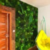 Green jungle moss and fern wall panel installed beside a wooden door with a yellow hanging chair