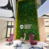 Large vertical preserved moss wall with white logo in a commercial lobby lounge with modern chairs.