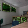 Three illuminated green moss wall art panels hung on an office wall above chairs and a reception counter.