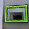Rectangular backlit moss mirror with dark wooden frame and illuminated LED strip on a tiled wall.
