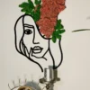 Woman line art with pink and green preserved moss on a wall above a silver candlestick and decorative eye mirror.