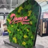 Curved green moss display on wheeled metal stand with pink 3D Domo interier logo lettering in a showroom.