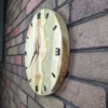 Round maple wood wall clock with mother-of-pearl epoxy resin, side view on a brick wall