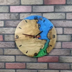 Round wall clock of light wood and blue-green epoxy resin, with black hands and markers, on a multi-colored brick wall.