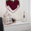Red moss heart wall decor mounted above a white dresser with a decorative lantern and lamp in a bedroom.