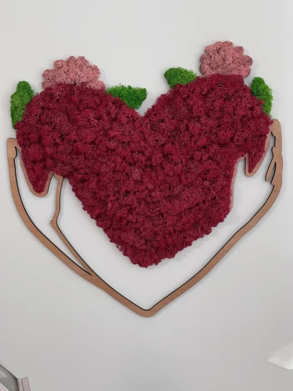 Heart-shaped preserved moss wall art framed by a wooden outline of embracing arms on a white wall.