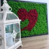 Framed green moss wall art with red double heart design, set on a wooden surface next to an ornate white lantern.