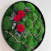 Round moss wall art with green moss, vibrant red roses, and rustic branches in a black circular frame.