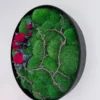 Side view of circular moss wall art with black frame, preserved green moss, branches, and red roses.