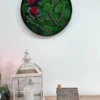 Round moss wall art with red roses and branches on a wall above a decorative white lantern and miniature house
