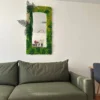 Vertical moss-framed mirror with preserved greenery mounted on a white wall above an olive green sofa.