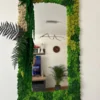 Rectangular mirror with green and beige reindeer moss frame and dark fern accents on a white wall.