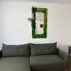 Rectangular moss wall mirror with preserved plants hanging above an olive green sectional sofa.