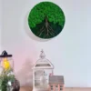 Round moss tree wall decor mounted on a white wall above decorative lanterns and a miniature house on a table.