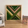 Natural wood framed wall art with green moss and wood diagonal inlays on a tabletop next to decor