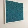 Teal blue reindeer moss wall art in a white frame mounted on a wall with power cord