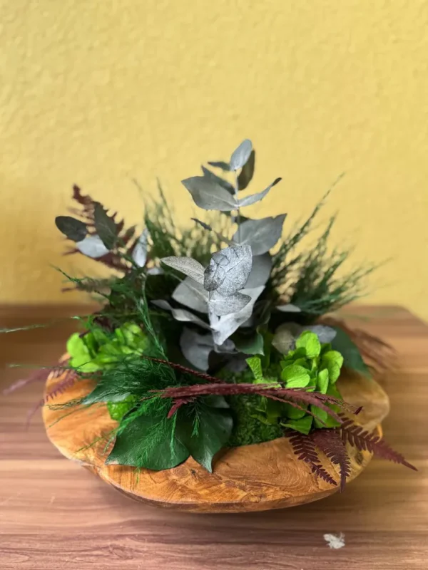 Wooden bowl centerpiece with preserved moss, ferns, and botanical foliage.