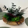 Wooden bowl (11.8") with green moss, eucalyptus leaves, and dark fern foliage on a dining table.