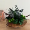 Rustic wooden bowl centerpiece filled with green moss, eucalyptus, and fern fronds on a table.