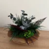 Top view of a rustic wooden bowl with preserved reindeer moss, eucalyptus stems, and ferns.