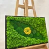 Framed green moss wall art featuring yellow pupil center, displayed on wooden easel