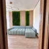 Two vertical rectangular green moss panels framed by light wood wall slats behind a sectional sofa.