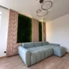 Preserved green moss wall panel inset into vertical wood slat paneling behind a light blue sectional sofa.
