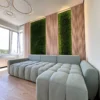 Vertical green moss wall panels integrated into light wood slat paneling behind a gray tufted sectional sofa.