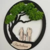 Angled view of round black wall art with green preserved moss canopy, wooden family silhouettes, and engraved plaque