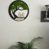 Round black tree wall art with green preserved moss hanging on a white wall above a potted houseplant.
