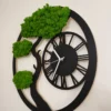 Side view of black round tree wall clock with green reindeer moss foliage and white clock hands
