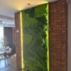 Illuminated vertical preserved moss wall panel installed between exposed brick pillars.