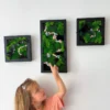 Child pointing toward a three-piece floral moss wall art set in black frames hanging on a white wall