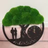 Black tree of life clock with green bun moss canopy, gold hands, and couple silhouette against a pink backrest.