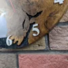 Close-up of oak and black resin wall clock with white numerals mounted on a textured brick wall.