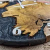 Close-up perspective of round oak clock showing textured wood grain, swirling black resin, and raised white numbers