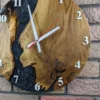 Round oak wall clock with black swirl epoxy resin, white numbers, and hands, mounted on a brick wall