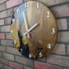 Round oak wall clock with black swirling epoxy resin and white numerals, mounted on a brick wall