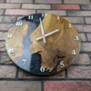 Front view of oak wall clock with black swirled epoxy resin and white Arabic numerals on a brick wall