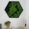 Hexagon green moss wall clock in a black wooden frame mounted on a white wall above tabletop decor.