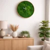 Round green moss wall clock with natural wood frame hanging above a wooden cabinet in a living room.